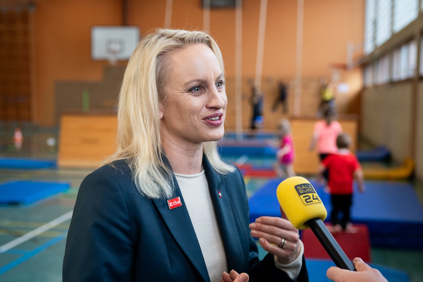 Sport-Staatssekretärin Michaela Schmidt gibt in einer Turnhalle ein Interview; im Hintergrund bewegen sich Kinder.