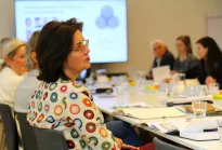 Dr.in Brigitte Zarfl im Gespräch bei der GÖG: Die Eigentümervertreterin der GÖG sitzt an einem Konferenztisch und beteiligt sich aktiv am Austausch mit weiteren Teilnehmenden. Im Hintergrund ist eine Präsentation zu sehen.