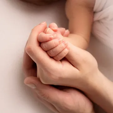 Babyhand in schützender Erwachsenhand – Symbol für Fürsorge.