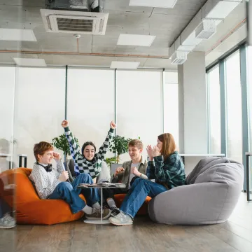 © Serhii - stock.adobe.com Vier Jugendliche sitzen entspannt auf Sitzsäcken in einem hellen Raum, lachen und feiern gemeinsam – Symbol für Gemeinschaft und psychische Gesundheit in der Schule.