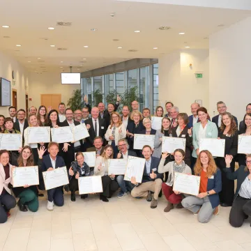 © Monika Fellner Gruppenfoto der Preisträger:innen des Best Practice Award „Klimafreundliche Gesundheitseinrichtungen“ 2025. Etwa 40 Personen halten Urkunden und feiern gemeinsam bei der Preisverleihung im Bundesministerium in Wien.
