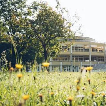 © A. ö. Krankenhaus des Deutschen Ordens Friesach GmbH Begrünte Außenanlage einer Gesundheitseinrichtung mit Blumenwiese, Bäumen und einem hellen Gebäude im Hintergrund.