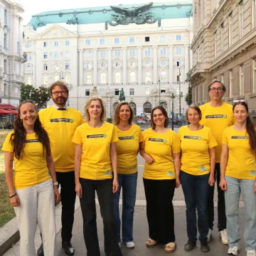 Acht Personen im gelben T-Shirt posieren vor der Wiener Ringstraße für ein Gruppenbild.