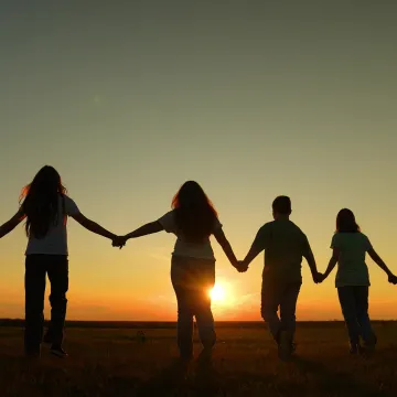 © TO LOVE - stock.adobe.com Sechs Menschen gehen bei Sonnenuntergang Hand in Hand über ein Feld. Das Bild steht für Gemeinschaft und soziale Verbundenheit.