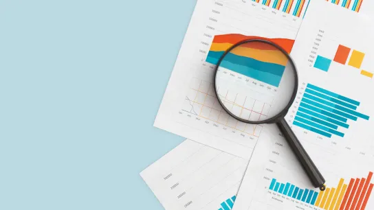 © LunaKate - stock.adobe.com Lupenansicht auf bunte Diagramme und Grafiken, die auf mehreren Papierblättern liegen.