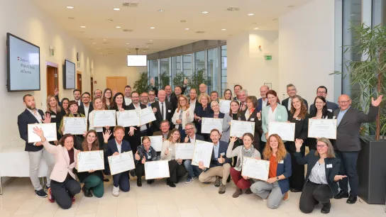 Gruppenfoto der Preisträger:innen des Best Practice Award „Klimafreundliche Gesundheitseinrichtungen“ 2025. Etwa 40 Personen halten Urkunden und feiern gemeinsam bei der Preisverleihung im Bundesministerium in Wien.