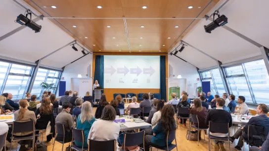 Teilnehmende sitzen im Konferenzsaal und verfolgen einen Vortrag zur Kreislaufwirtschaft im Gesundheitswesen auf der Bühne.