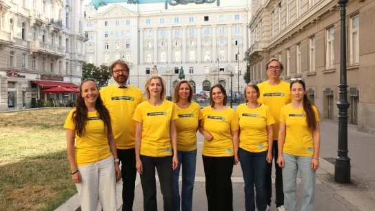 Acht Personen im gelben T-Shirt posieren vor der Wiener Ringstraße für ein Gruppenbild.